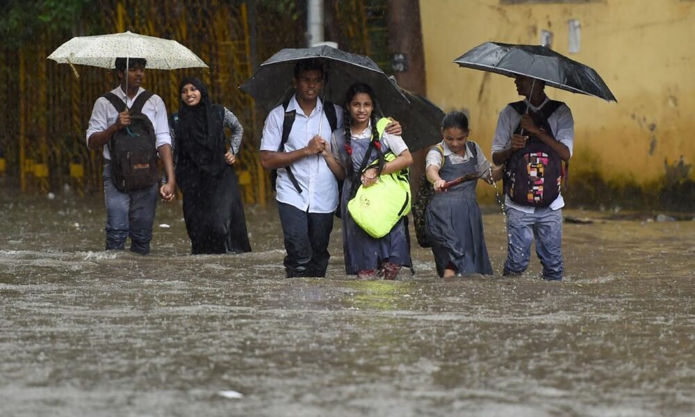 Students walking with umbrellas during heavy rainfall in Mumbai.