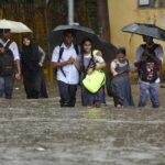 Students walking with umbrellas during heavy rainfall in Mumbai.