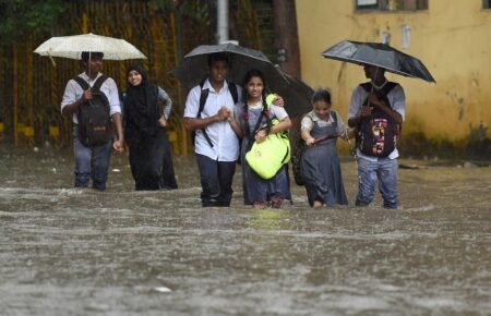 Students walking with umbrellas during heavy rainfall in Mumbai.